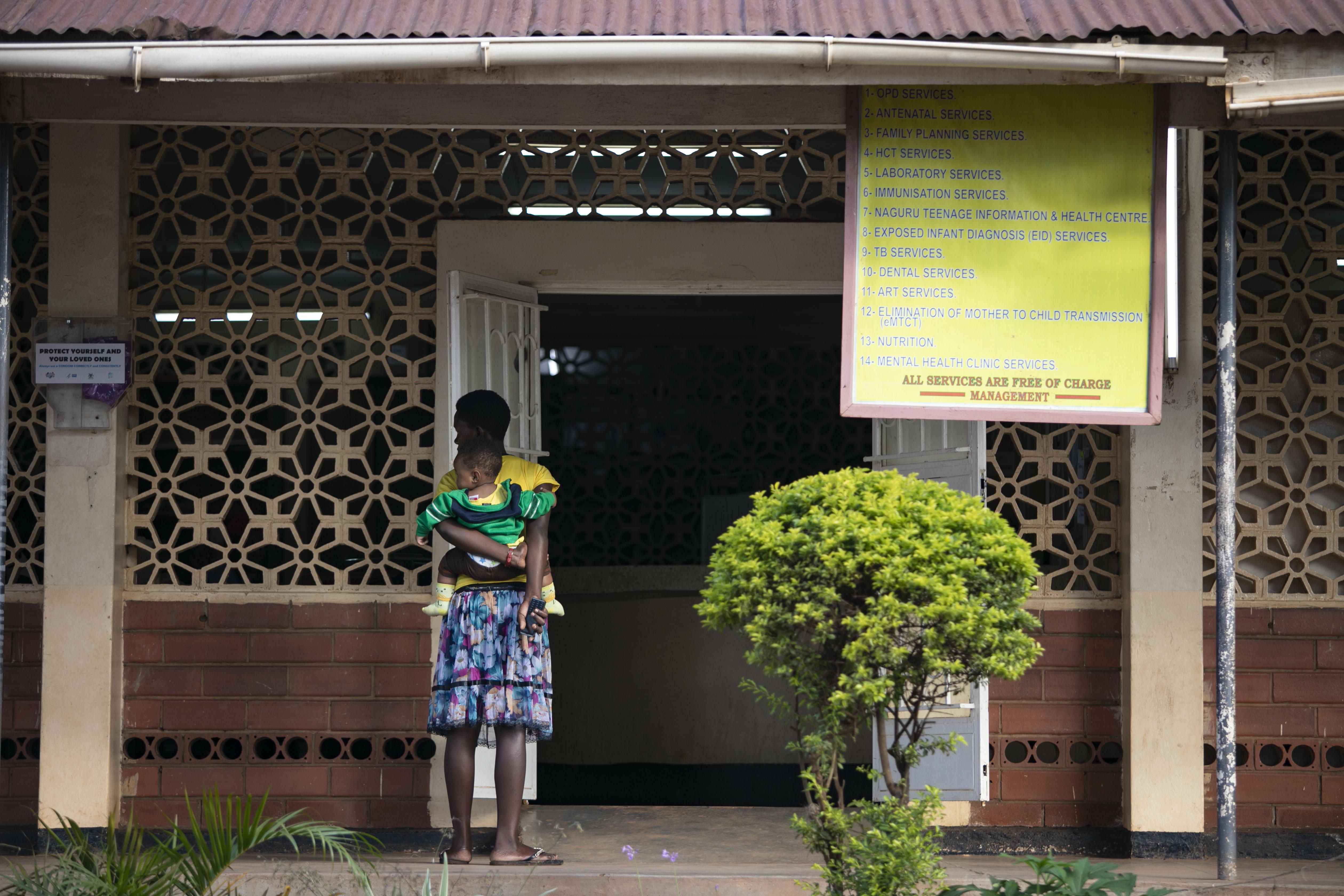 Woman with baby on her back and standing in front of a Ugandan facility